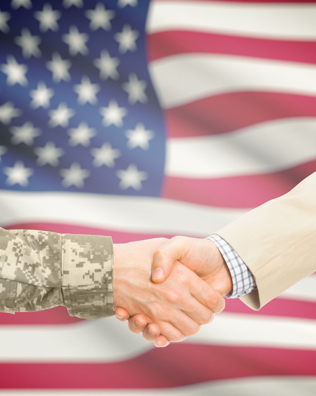 American soldier in uniform and civil man in suit shaking hands with national flag on background - United States